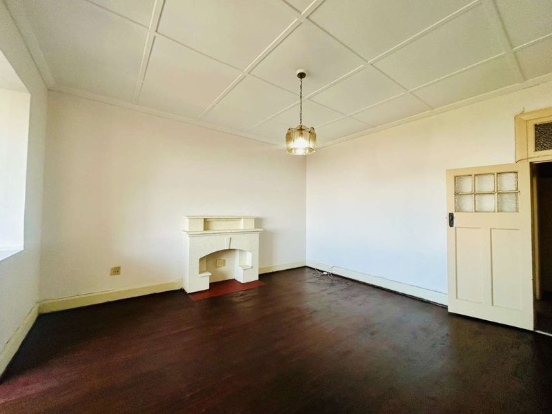 An empty living room featuring dark timber flooring, a traditional fireplace, and a classic tiled ceiling, offering a blank canvas for renovation.