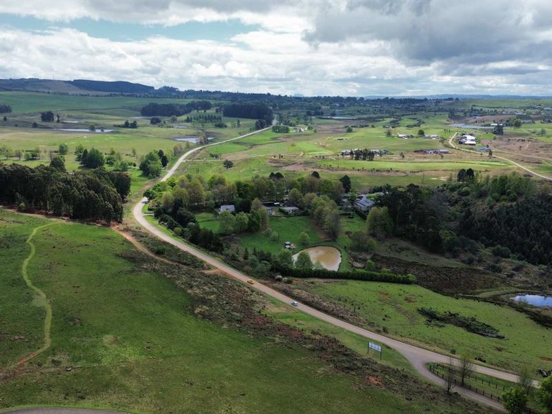 An aerial view of a vast, green rural landscape featuring rolling hills, a winding road, and natural water features.