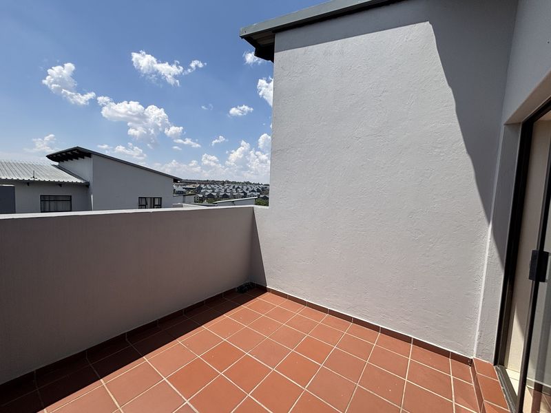 A private balcony featuring terracotta-style floor tiles and a solid parapet wall, offering an open outdoor space accessible from the interior.