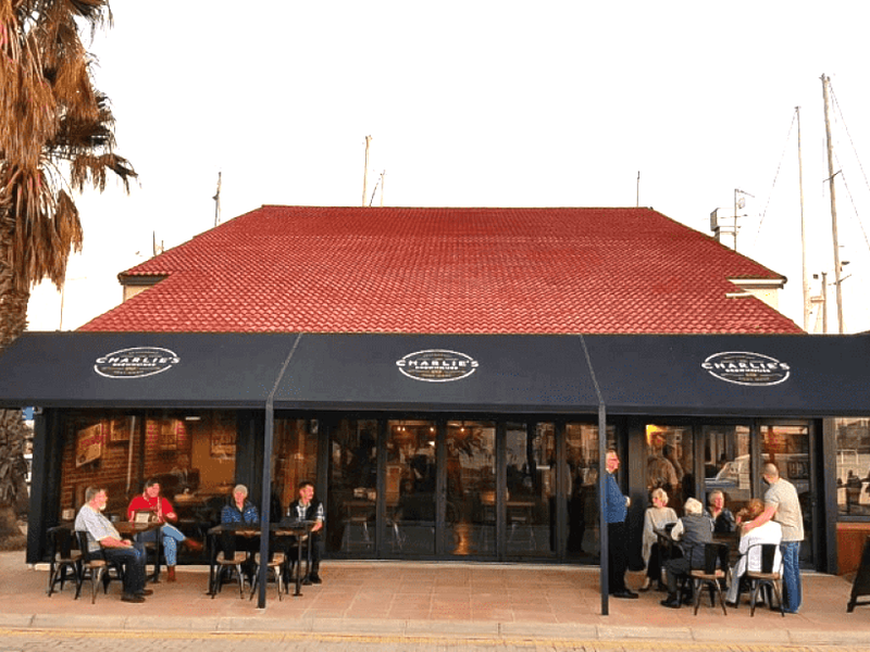 Front elevation of a commercial property featuring a red tiled roof, large black awning, and folding glass doors opening onto a paved patio area.