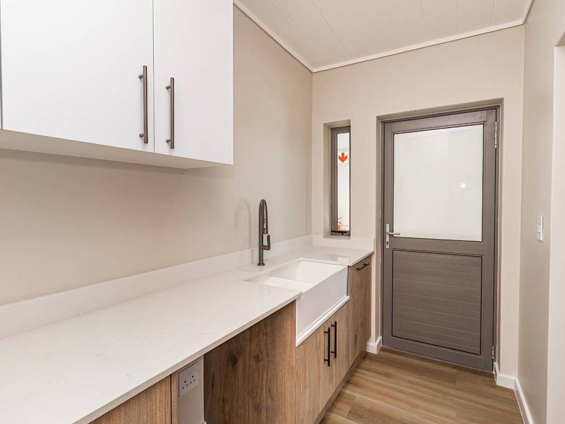 A modern, clean laundry room featuring white quartz countertops, a farmhouse sink, wood-look cabinetry, and direct access to the exterior.