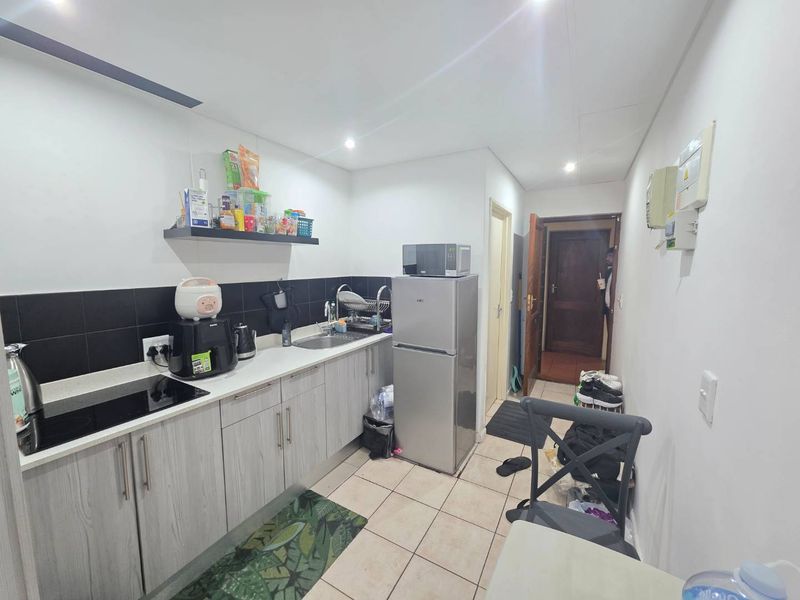 Compact kitchen featuring light wood-grain cabinetry, black tiled backsplash, laminate countertops, and integrated sink, providing a functional workspace.