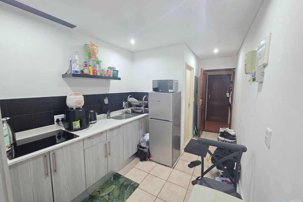 Compact kitchen featuring light wood-grain cabinetry, black tiled backsplash, laminate countertops, and integrated sink, providing a functional workspace.