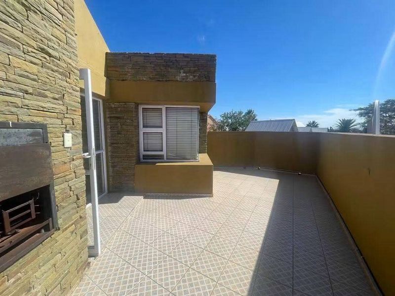 A spacious outdoor patio featuring tiled flooring, stone cladding accents, and a built-in braai area, perfect for outdoor entertaining.