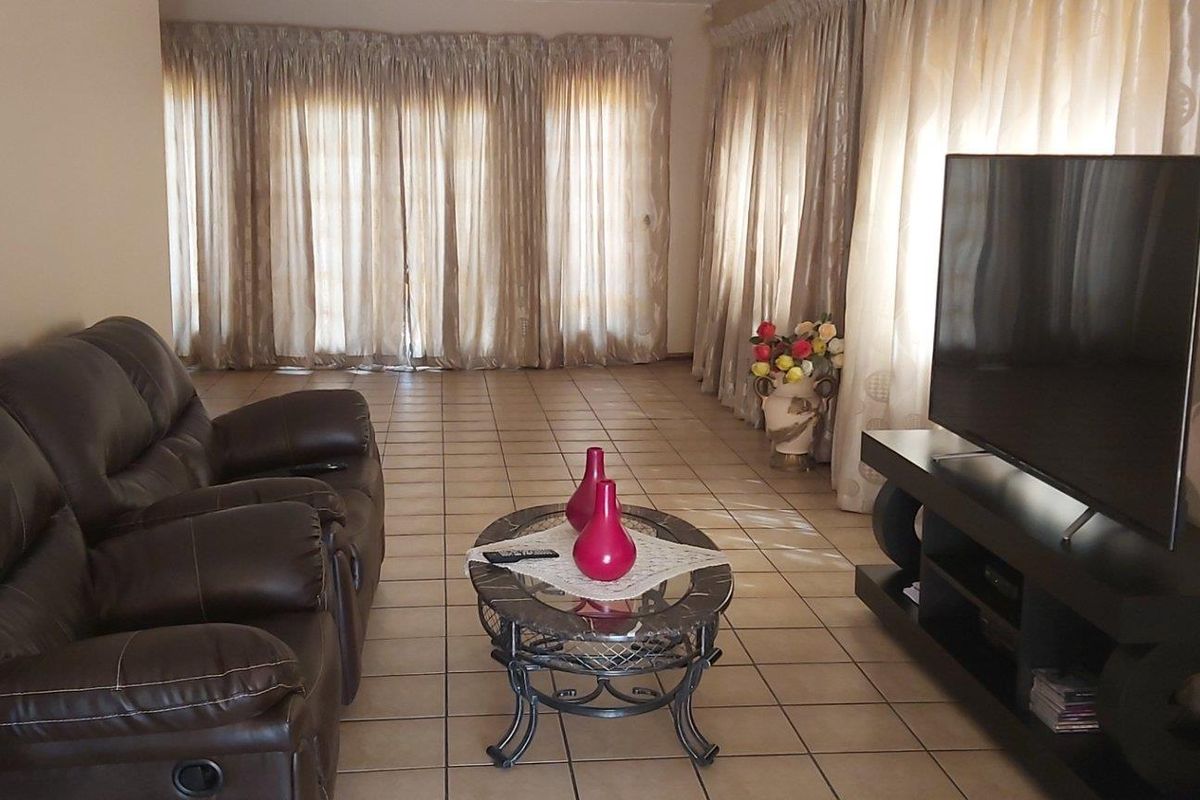 Spacious living room featuring tiled flooring and large windows with floor-to-ceiling curtains, providing ample natural light.