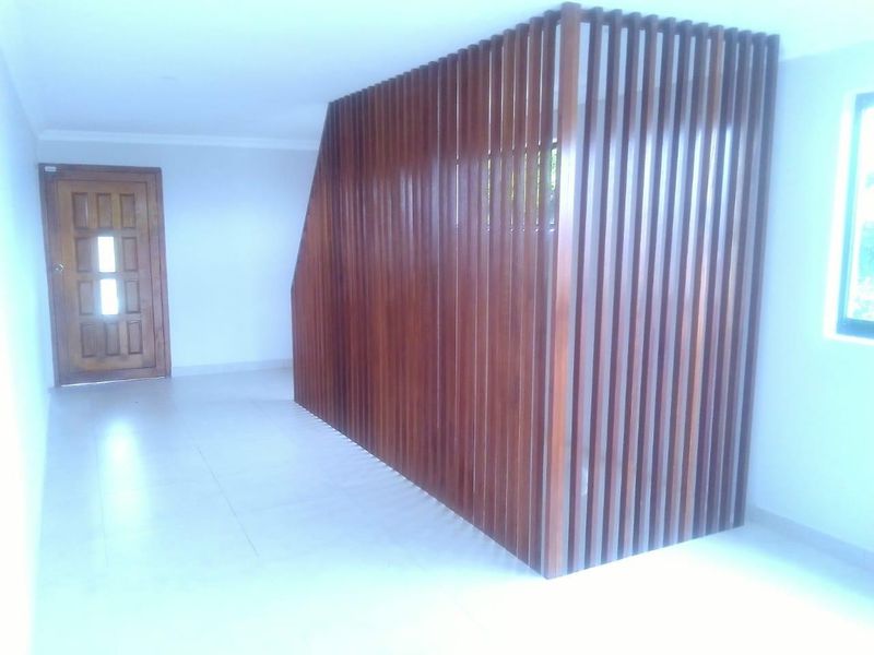A bright, empty hallway featuring tiled flooring, a timber panelled entrance door, and a decorative timber slat room divider.