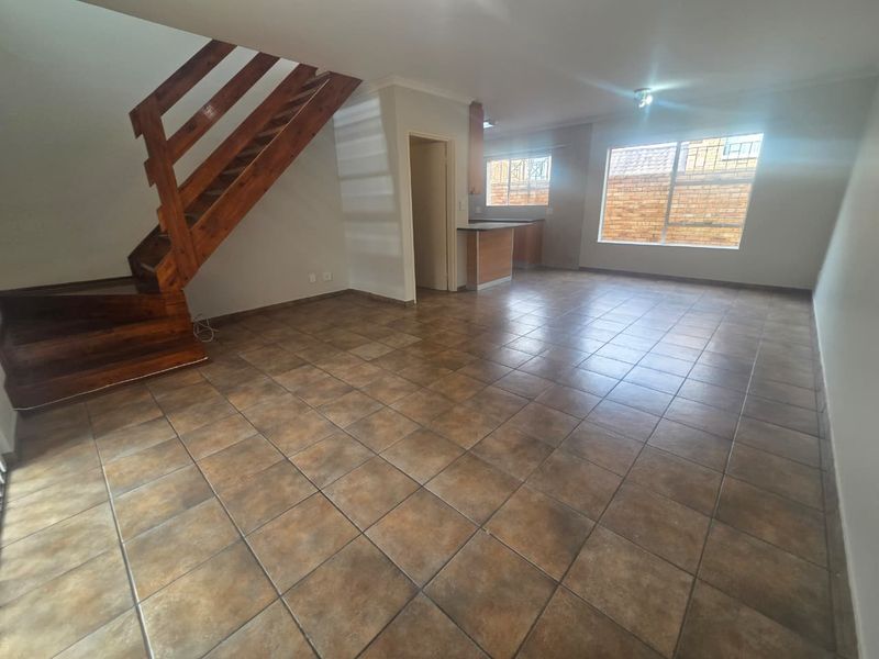 Spacious open-plan living area featuring ceramic floor tiles, a wooden staircase, and an adjoining kitchen space with built-in cabinetry.