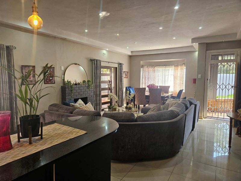 Spacious open-plan living and dining area featuring tiled floors, recessed lighting, and a brick fireplace, with direct access to the exterior.
