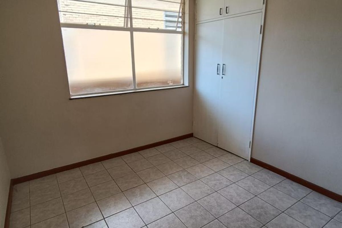 An empty bedroom featuring tiled flooring, a built-in wardrobe, and a window with security bars, offering a blank canvas for potential updates.