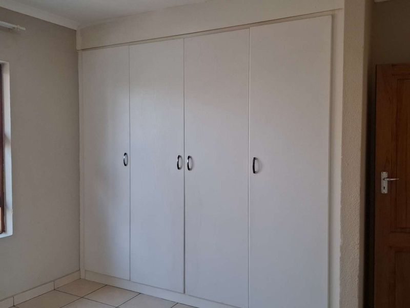 A clean, empty bedroom featuring neutral walls, tiled flooring, and ample built-in cupboard storage with a window providing natural light.