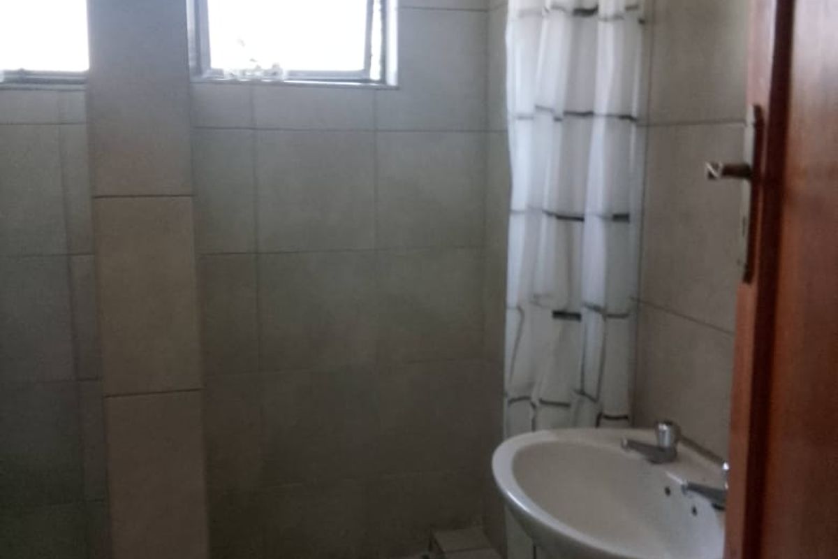 A functional bathroom featuring a pedestal basin, tiled shower enclosure, and tiled walls, requiring some maintenance and cosmetic updates.