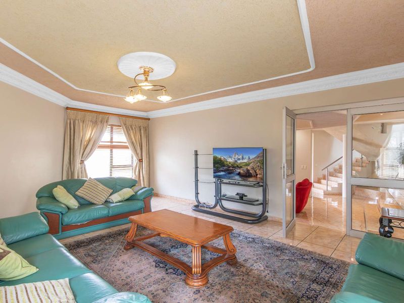 Spacious living room featuring tiled flooring, a decorative coved ceiling with a central ceiling rose, and glass-panelled doors leading to the hallway.