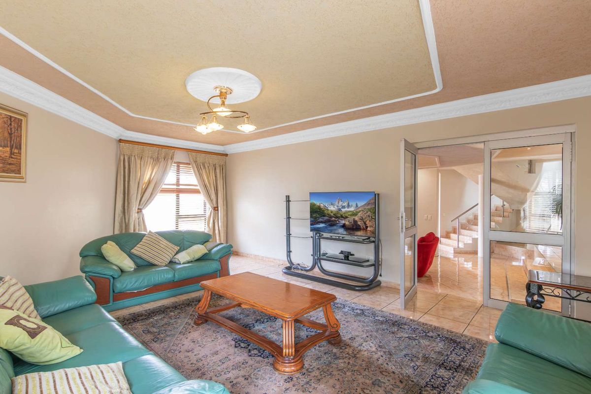 Spacious living room featuring tiled flooring, a decorative coved ceiling with a central ceiling rose, and glass-panelled doors leading to the hallway.