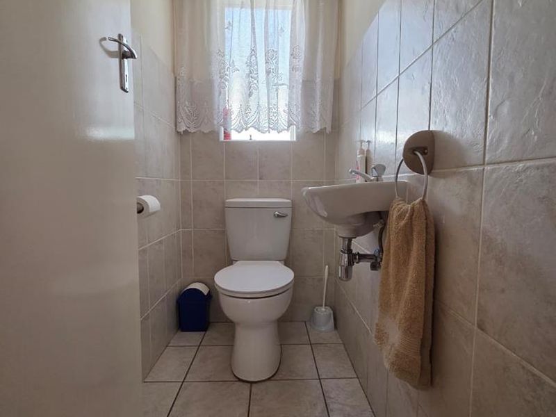A compact guest bathroom featuring neutral ceramic wall and floor tiles, a wall-mounted basin, and a standard toilet.