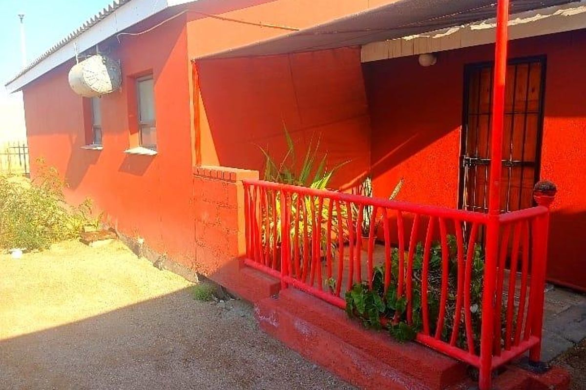 Rear exterior view of the property featuring a covered patio area with metal railings and a security gate entrance.