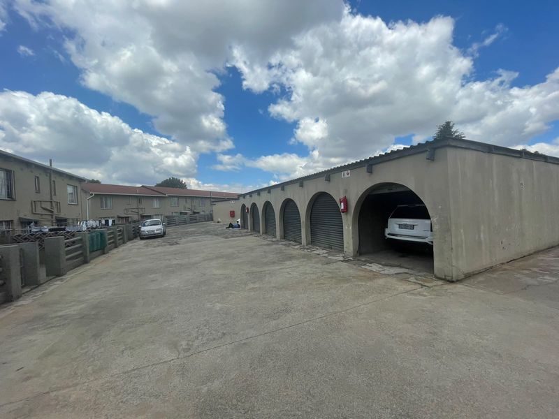 A row of arched garage bays with roller shutter doors situated along a concrete driveway in an apartment complex.