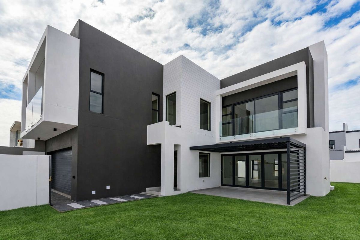 Modern double-story residence featuring a contemporary architectural design, glass balustrades, a covered patio area, and a well-maintained lawn.