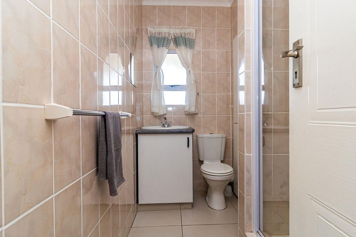 A compact bathroom featuring a vanity with basin, toilet, and a glass-enclosed shower, finished with neutral wall and floor tiles.
