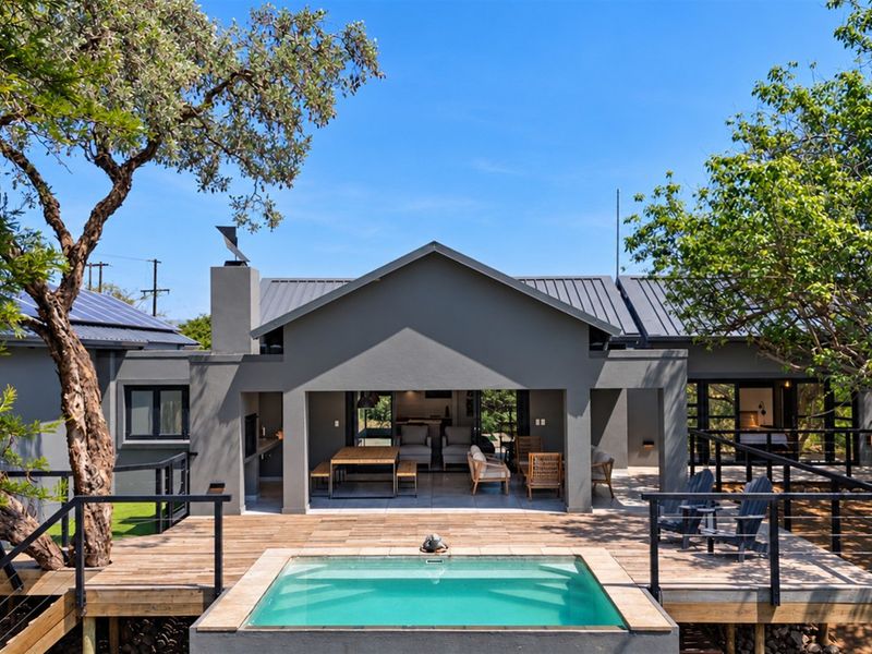 A well-maintained rear exterior featuring a modern covered patio, timber decking, and a swimming pool set against a contemporary grey-painted house facade.