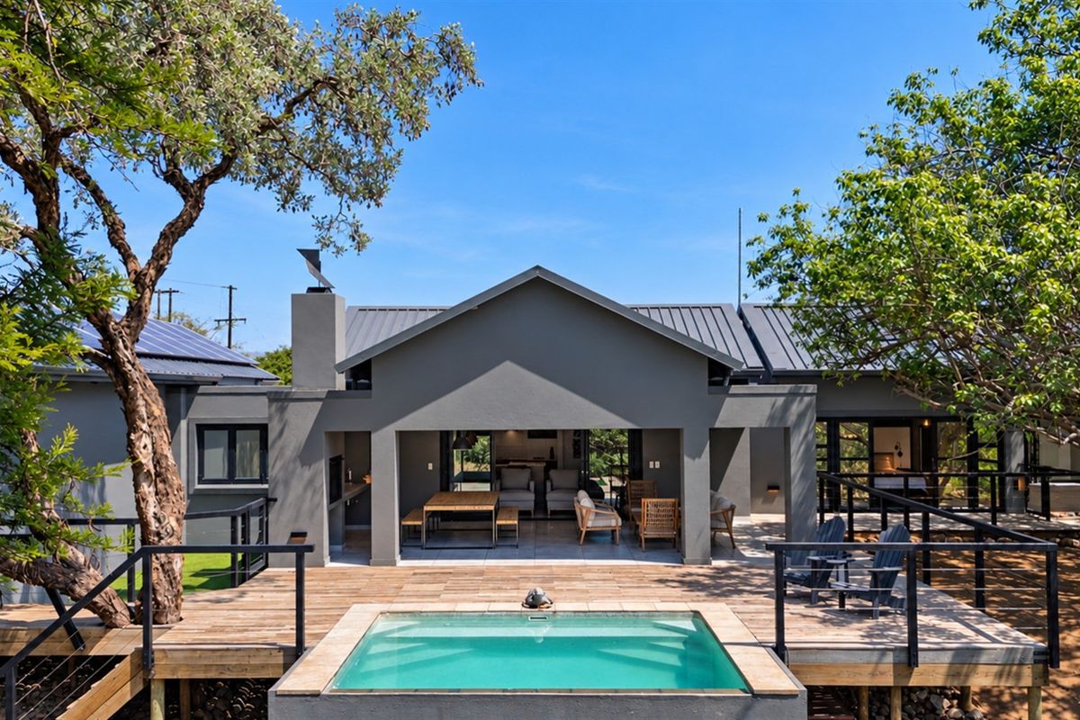 A well-maintained rear exterior featuring a modern covered patio, timber decking, and a swimming pool set against a contemporary grey-painted house facade.