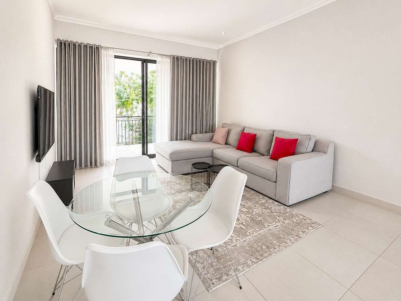 Bright open-plan living and dining area featuring neutral tiled flooring and a sliding glass door leading to a private balcony.