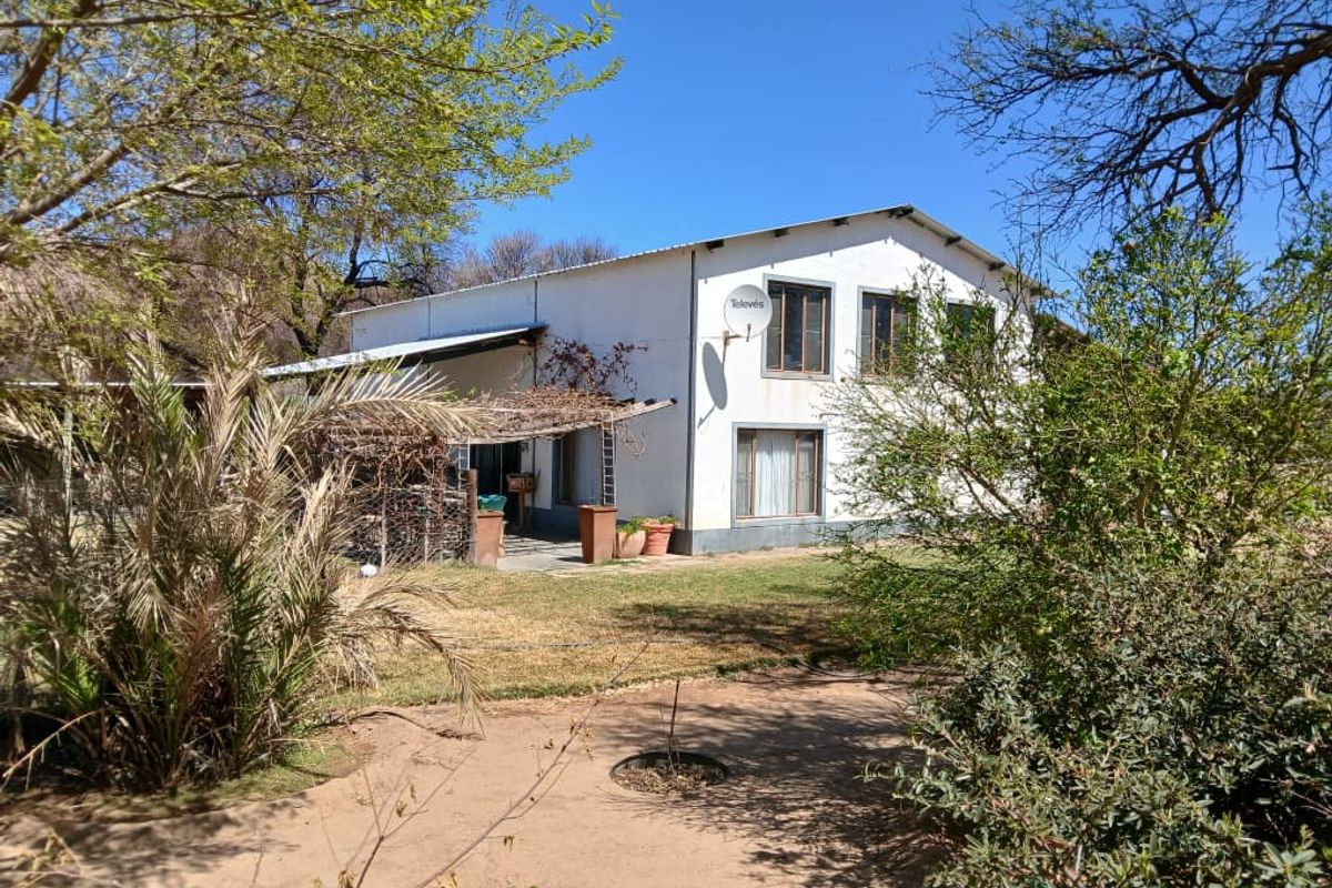 Rear view of the property featuring a white facade, metal roofing, and a covered patio area set within a garden landscape.