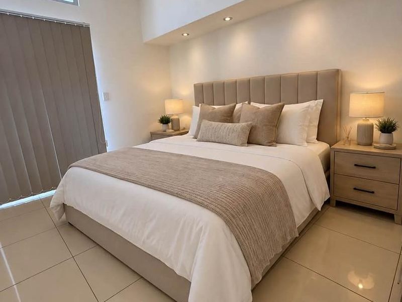 A modern, well-lit bedroom featuring neutral tiled flooring, a bulkhead ceiling with recessed lighting, and vertical blinds for privacy.