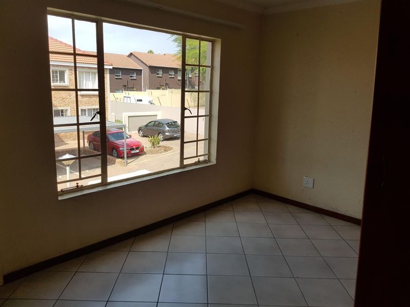 An empty bedroom featuring tiled flooring and a large window with views of the complex parking area.