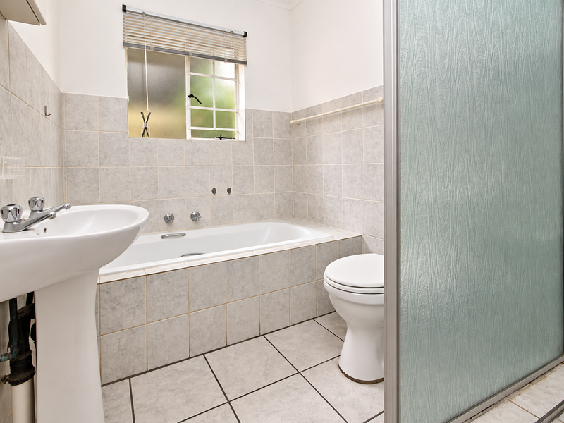 A functional bathroom featuring a pedestal basin, built-in bathtub, toilet, and a separate shower enclosure with tiled finishes throughout.