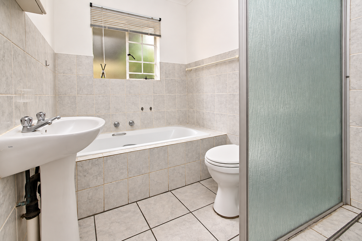 A functional bathroom featuring a pedestal basin, built-in bathtub, toilet, and a separate shower enclosure with tiled finishes throughout.