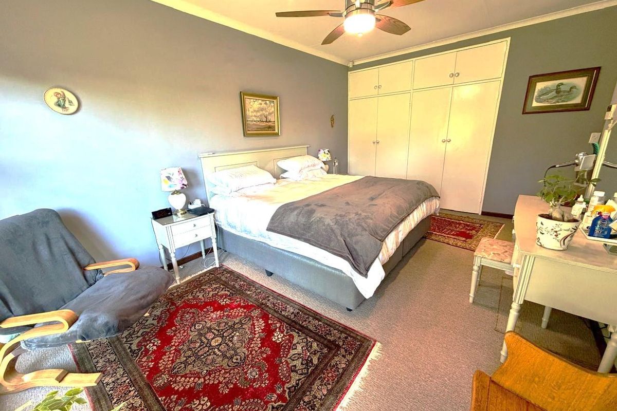A spacious bedroom featuring built-in cupboards, a ceiling fan, and neutral wall tones, offering a comfortable and functional living space.