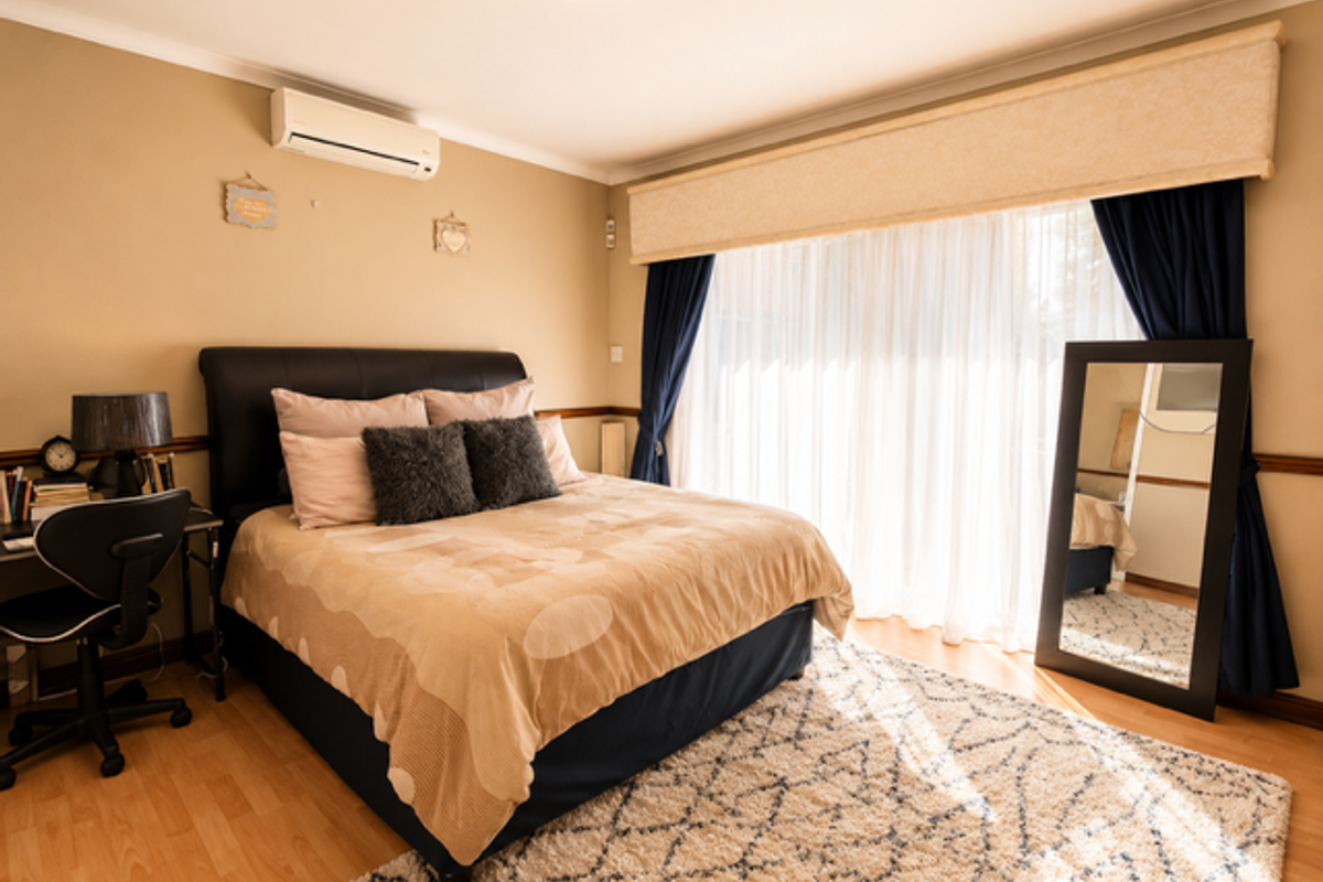 A well-maintained bedroom featuring laminate flooring, a split-system air conditioner, and large sliding glass doors that provide ample natural light.