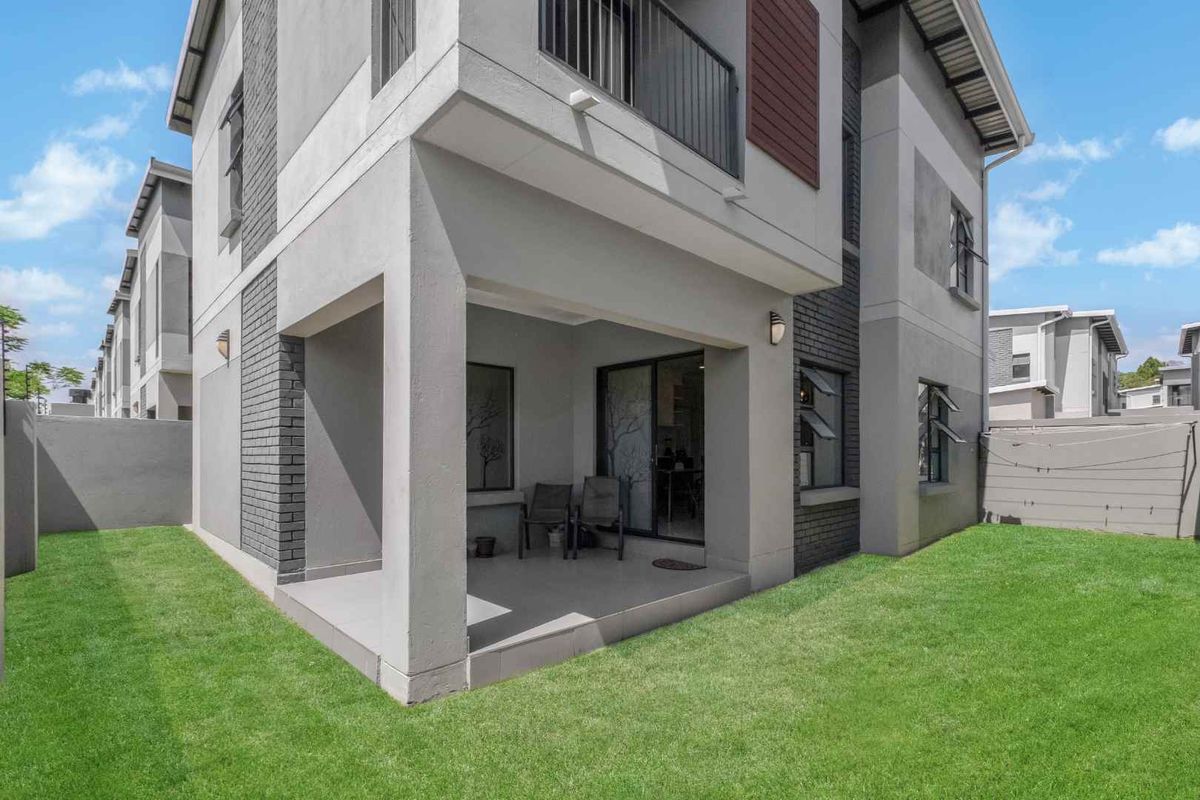 A modern rear exterior view of a cluster home featuring a covered patio, tiled flooring, and a private garden area.