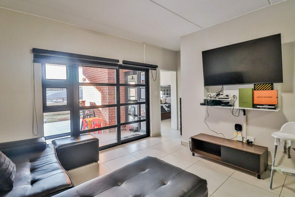 A bright living room featuring large black-framed glass sliding doors leading to an outdoor patio area and tiled flooring throughout.