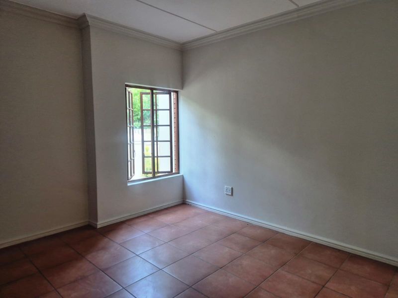 A bright, empty bedroom featuring neutral walls, tiled flooring, and a classic casement window with crown molding detail.