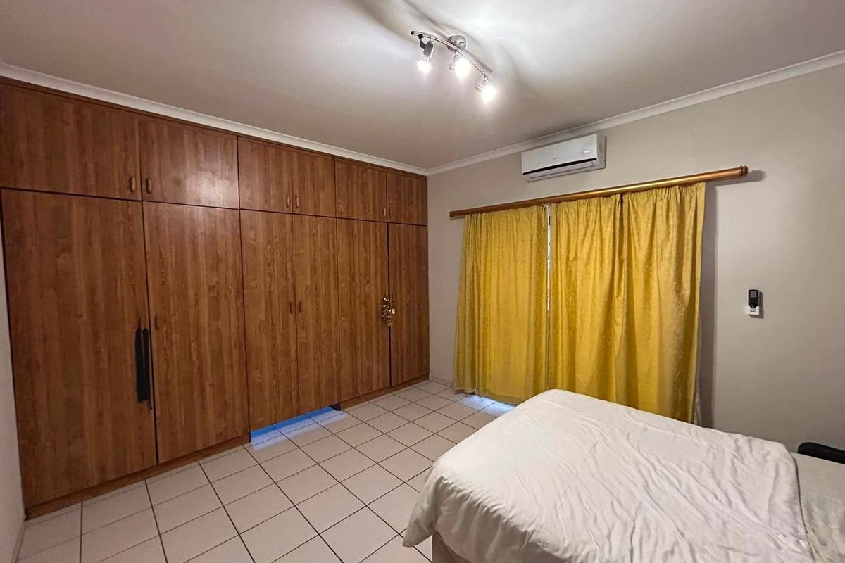 A bedroom featuring extensive built-in wooden cabinetry, tiled flooring, and a wall-mounted air conditioning unit.