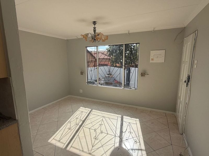 An empty living room featuring tiled flooring, a window with security bars, and a central ceiling light fixture.