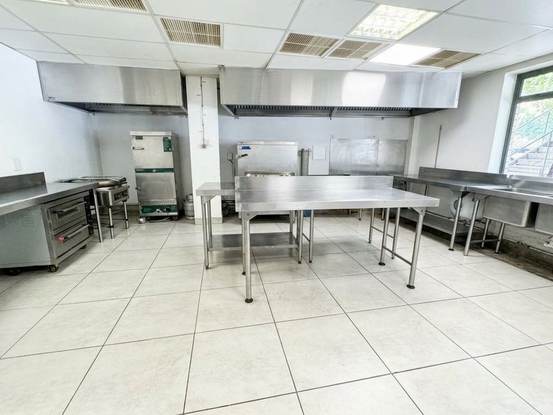 Commercial kitchen facility featuring stainless steel prep stations, industrial extractor hoods, a sink unit, and durable tiled flooring.