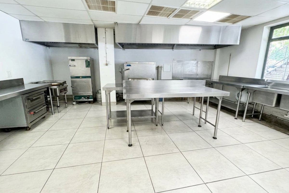 Commercial kitchen facility featuring stainless steel prep stations, industrial extractor hoods, a sink unit, and durable tiled flooring.