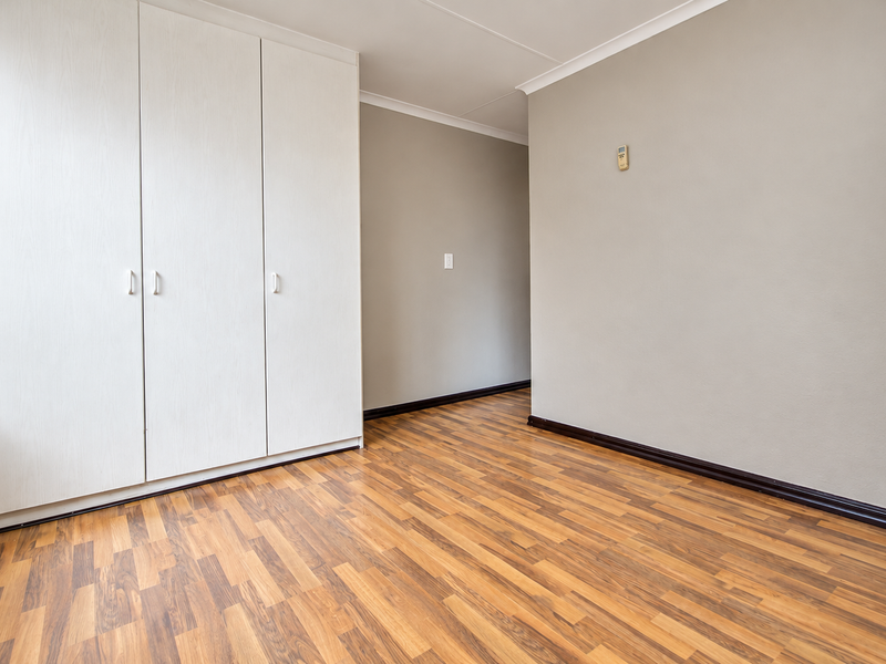 A clean, empty bedroom featuring neutral walls, laminate flooring, and built-in cupboards, offering a versatile space ready for personalization.