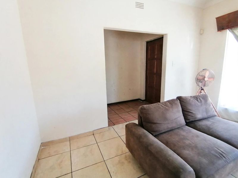 A living room area featuring ceramic tiled flooring and a wooden door leading to an adjacent space, showing signs of wear on walls and floors.