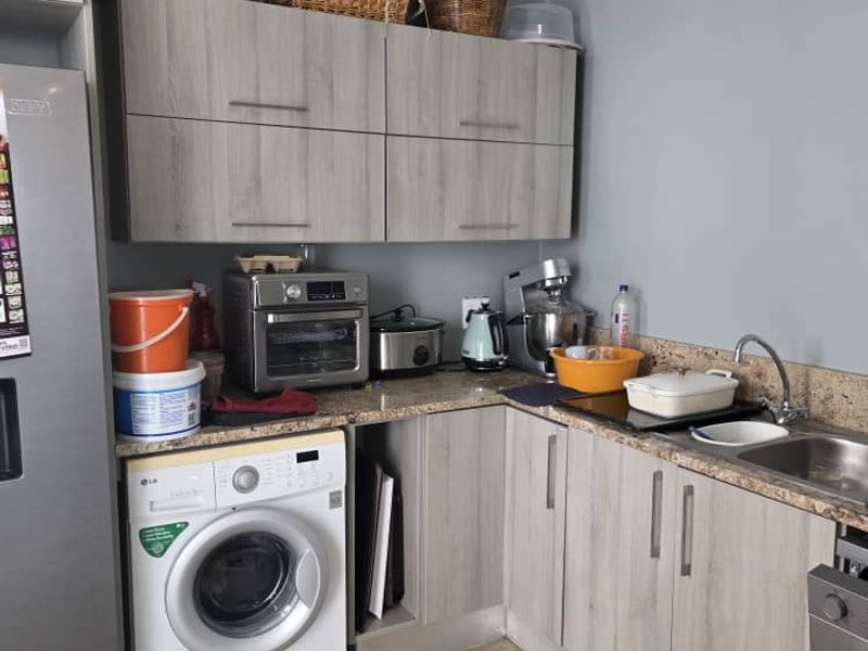 A functional kitchen area featuring light wood-look cabinetry, granite countertops, and tiled flooring, with an integrated space for laundry appliances.