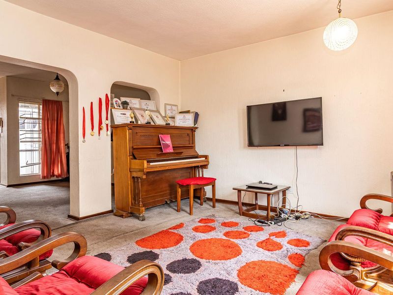A living room featuring an arched entryway, wall-mounted television, and carpeted flooring, providing a functional space with potential for modernization.
