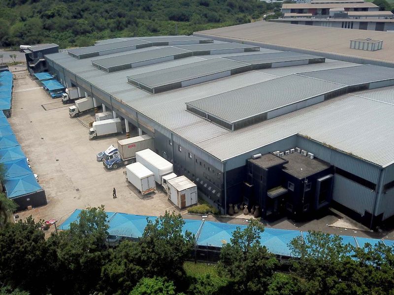 Aerial view of a large industrial warehouse facility featuring extensive loading bays, metal roofing with skylights, and a paved yard area.