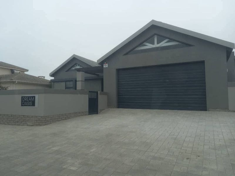 Modern front facade featuring a paved driveway, secure boundary wall with pedestrian gate, and a large automated garage door.