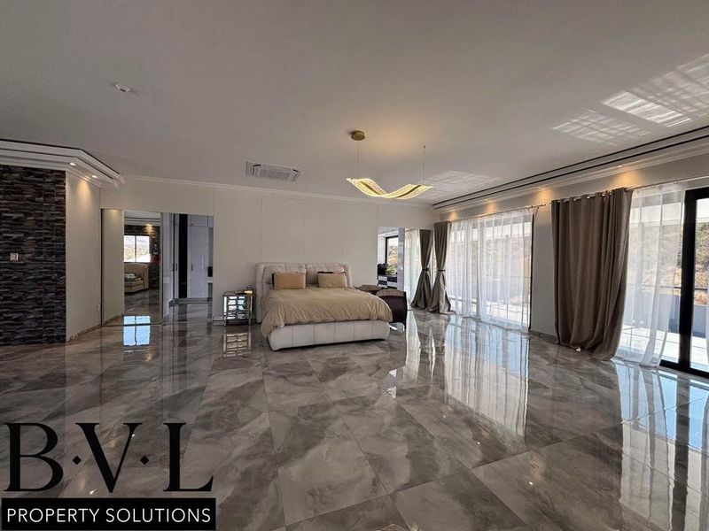 Spacious master bedroom featuring large format polished floor tiles, a stone feature wall, ducted air conditioning, and direct access to an outdoor area.