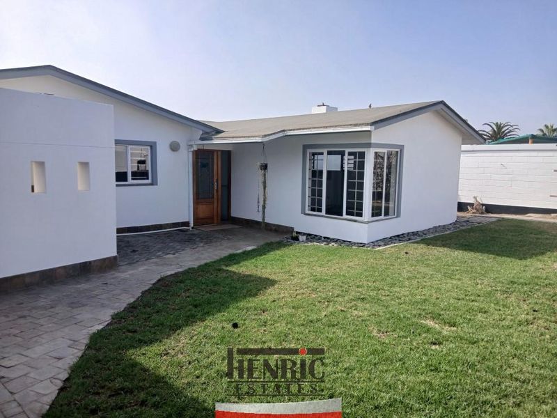 Rear view of the property featuring a paved walkway, well-maintained lawn, and a bay window overlooking the garden area.