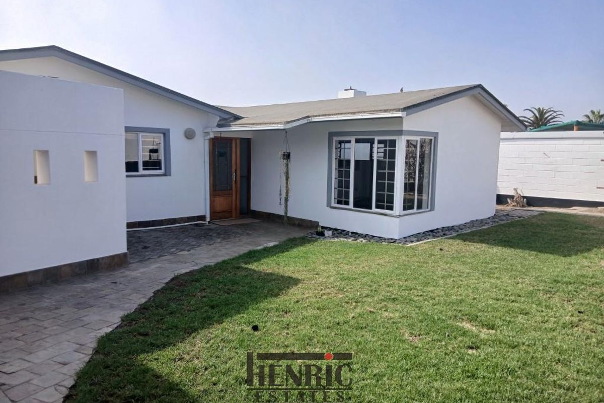 Rear view of the property featuring a paved walkway, well-maintained lawn, and a bay window overlooking the garden area.