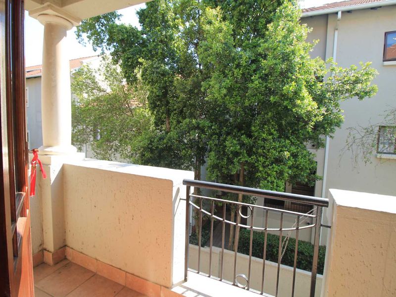 A private balcony featuring tiled flooring, a metal balustrade, and a structural pillar, overlooking mature trees and neighboring apartment buildings.