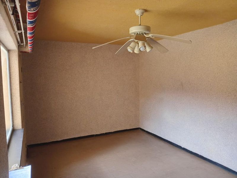 An empty bedroom featuring a ceiling fan, textured walls, and a window, offering a blank canvas for renovation and modernization.